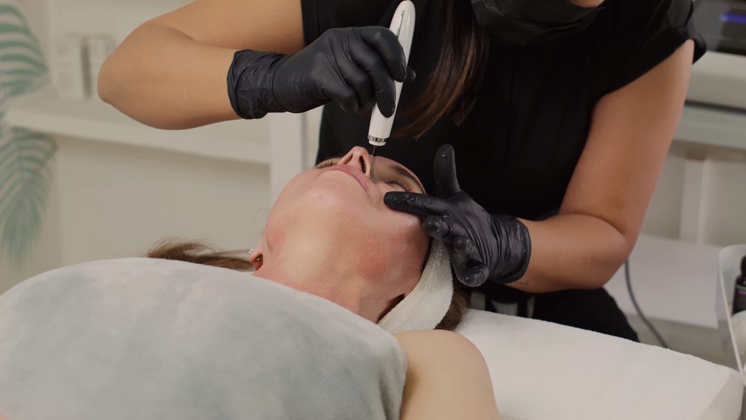 Close-up of gloved hands supporting a client’s face during a facial